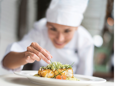 Cook decorating a plate and putting the ultimate touches - focus on foreground 